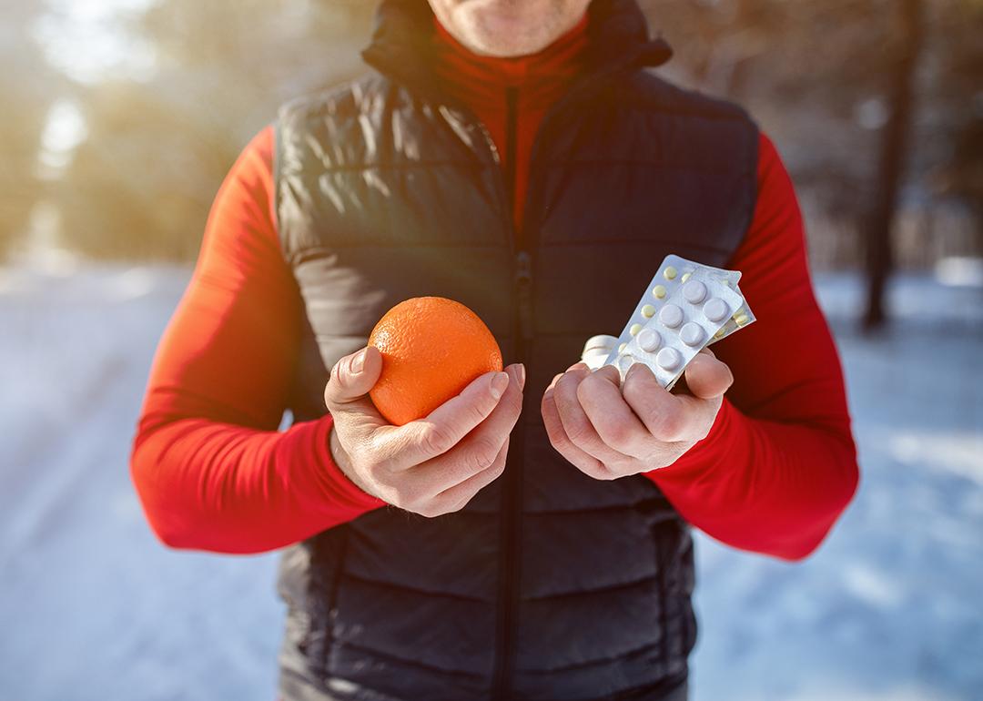 Cropped view of a sportsman holding an orange and pills outside during winter season.