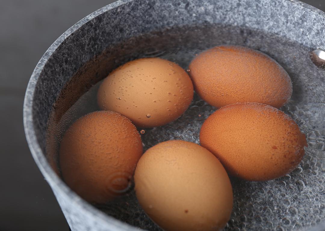 Five chicken eggs being boiled in a saucepan.