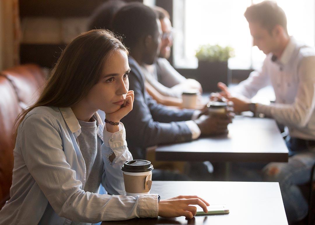 Young woman sits by herself at a coffee shop with drink in front of her.