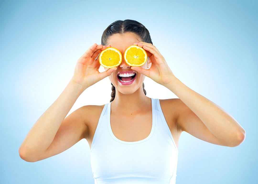 A woman holds orange slices over her eyes.