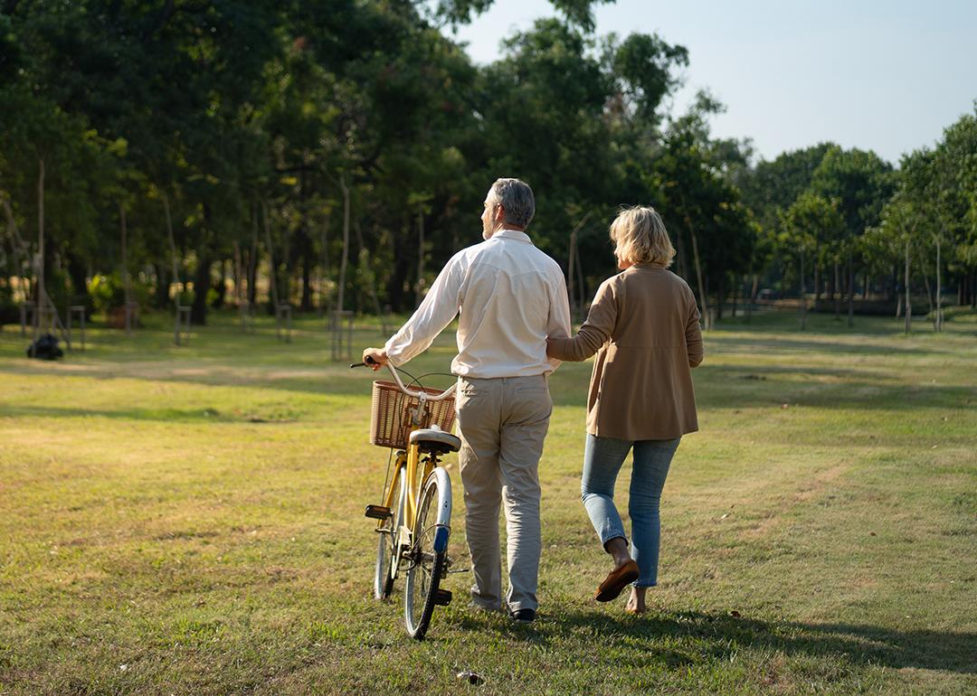 A middle-aged couple taking a stroll in a wide park with a bike.