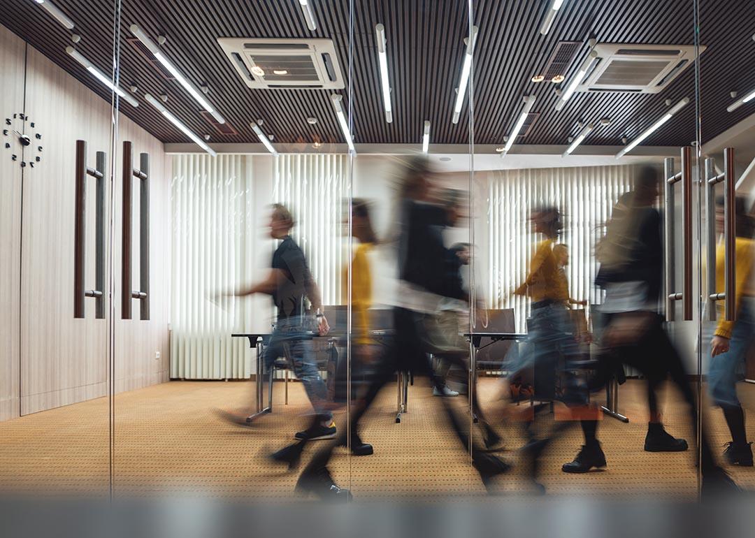 Photo of motion-blurred employees walking in front of office conference room.