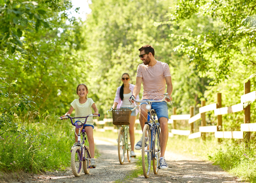 A family consisting of a father, mother and young daughter biking through a green wooded park