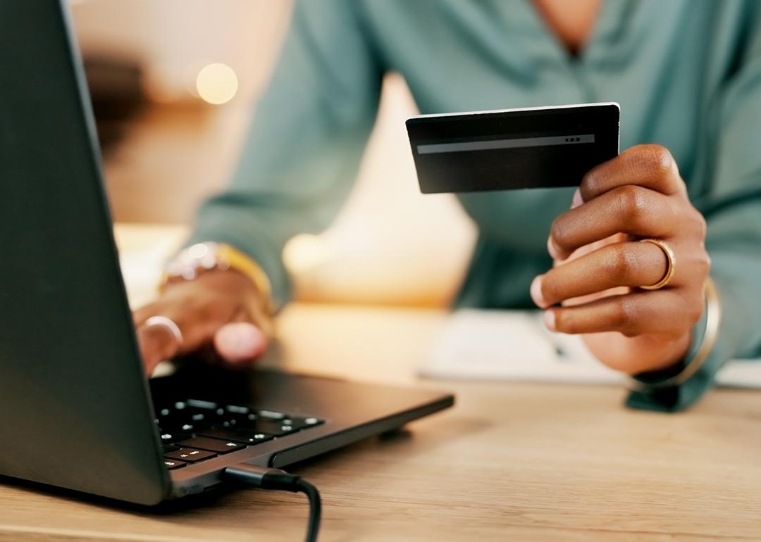 A female employee holding a company card for a transaction using a laptop.