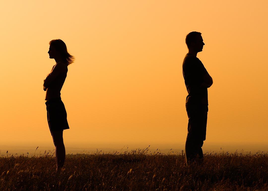 Concept of relationship difficulties shown through silhouettes of two people facing away from each other with orange sunset-colored background.