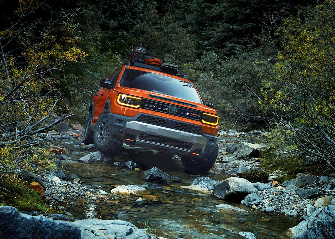 An orange 2026 Honda Passport on a rocky river road.