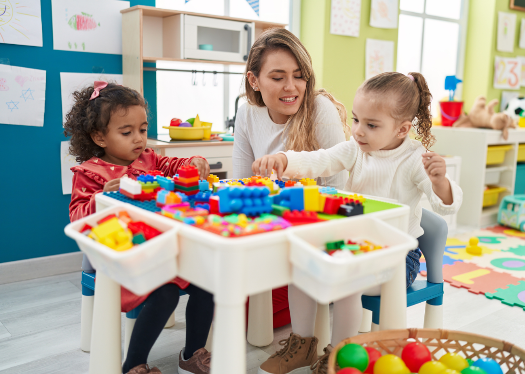 Kindergarten teacher sitting with two children playing with construction blocks in a classroom