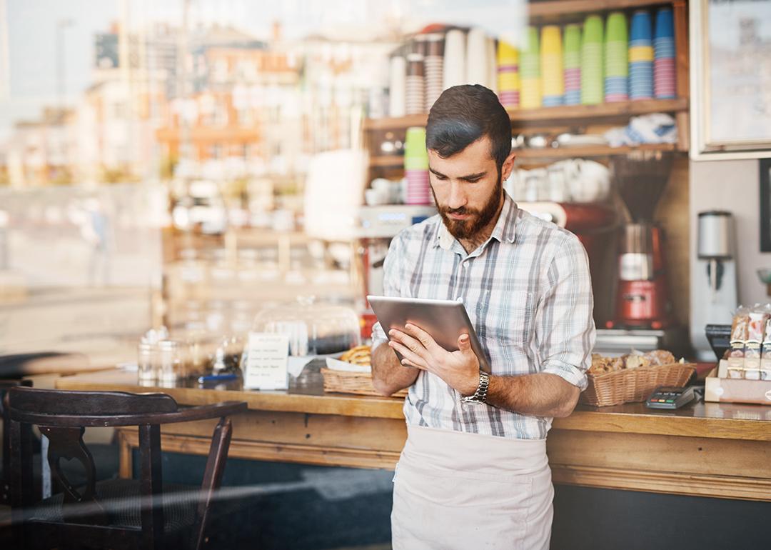 A coffee shop owner using his tablet by the counter.