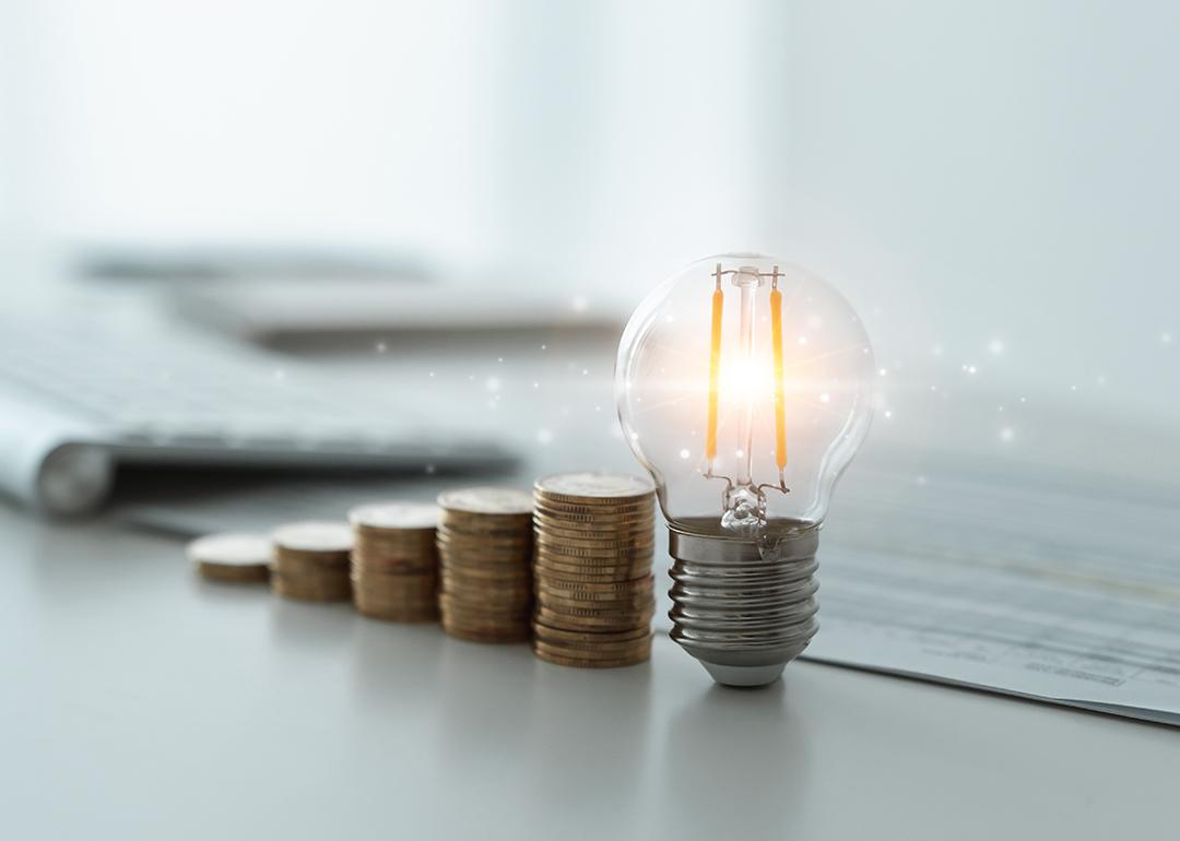 A light bulb and rows of coins decreasing against the background of financial reports as a concept of reducing tax costs.