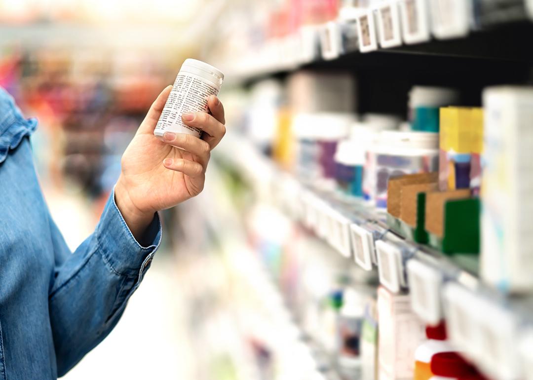 A customer carefully reviewing bottle of medicine from an aisle during a purchase.