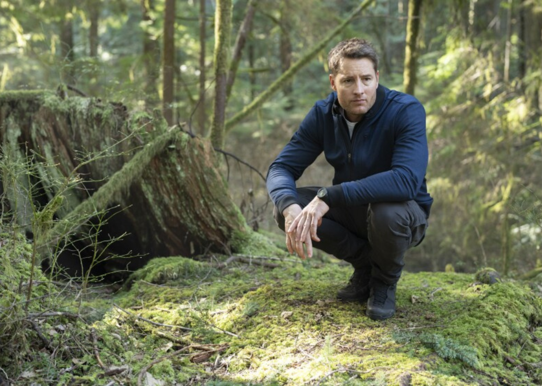 Justin Hartley crouching down on a mossy forest floor in a scene from 'Tracker' (2024)