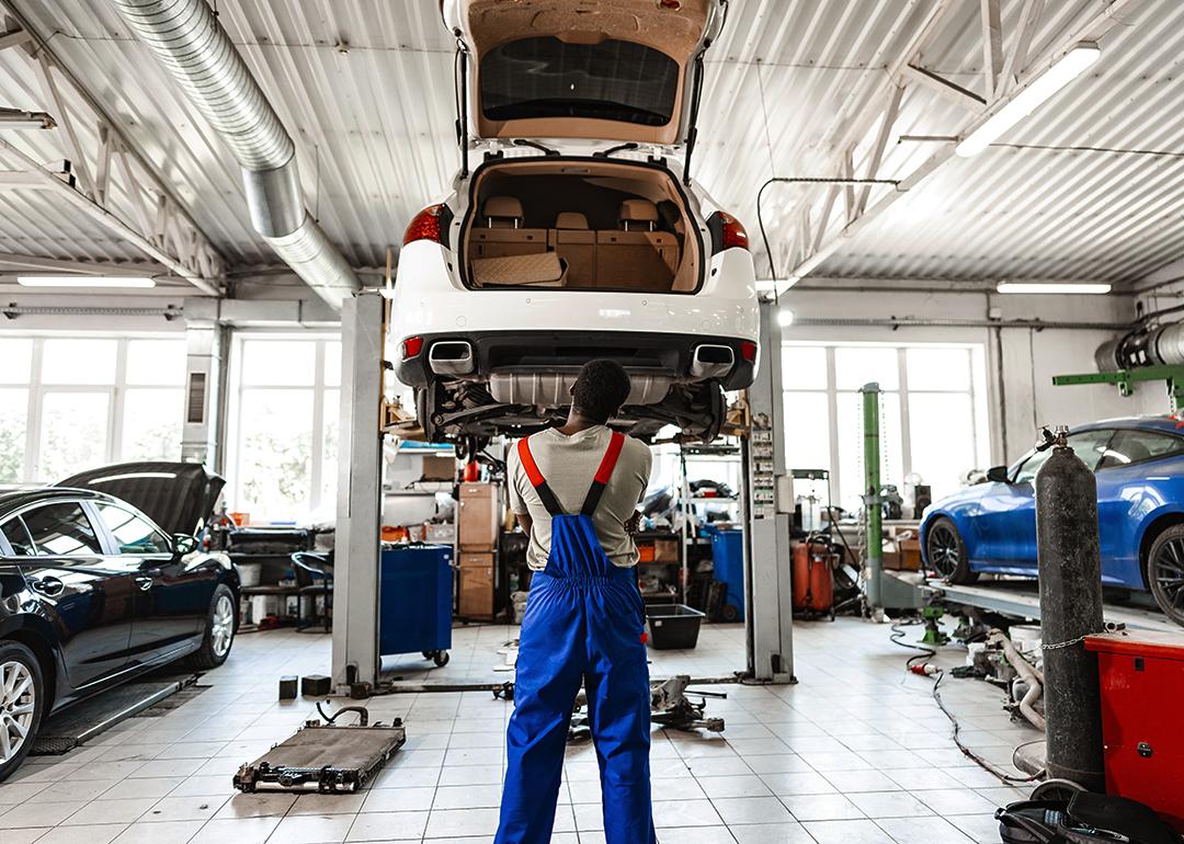 A pensive mechanic in a car service looking up a lifted car for repair.