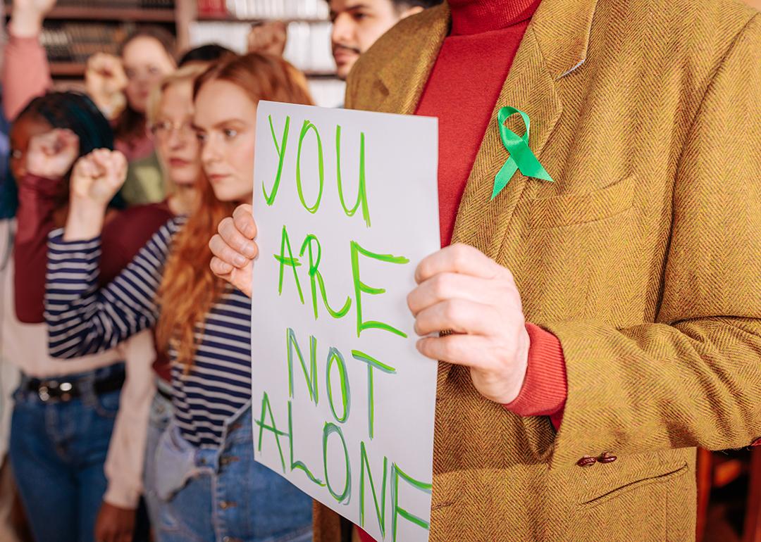 Young adults and a mental health counselor wearing a green ribbon and holding up a "you are not alone" sign to drive support during Mental Health Awareness month.