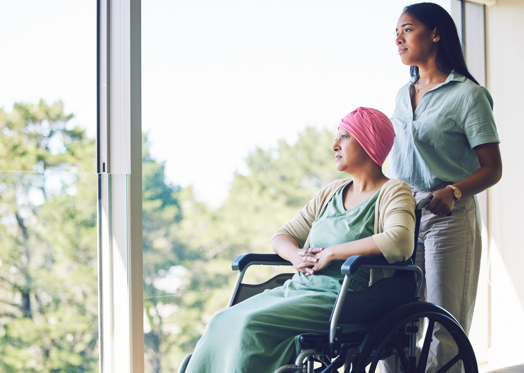 A woman in her 30s pushes another older woman in a wheelchair down a hallway.