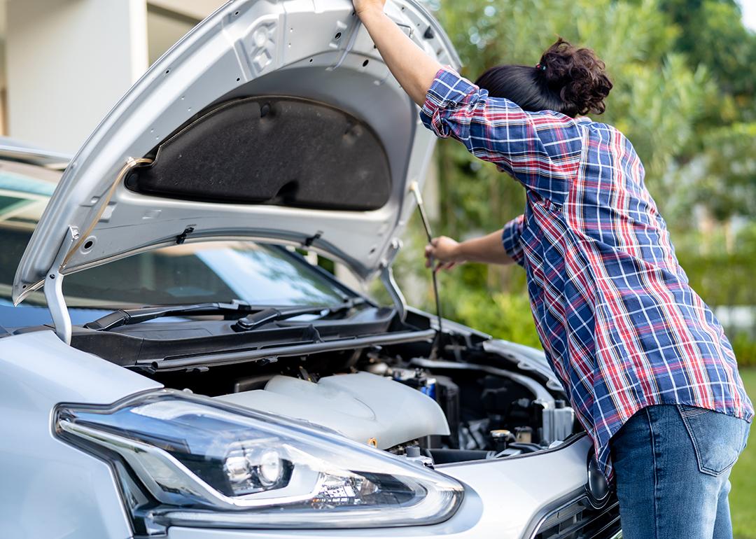 A female car owner opening the hood of her silver car to inspect its engine.