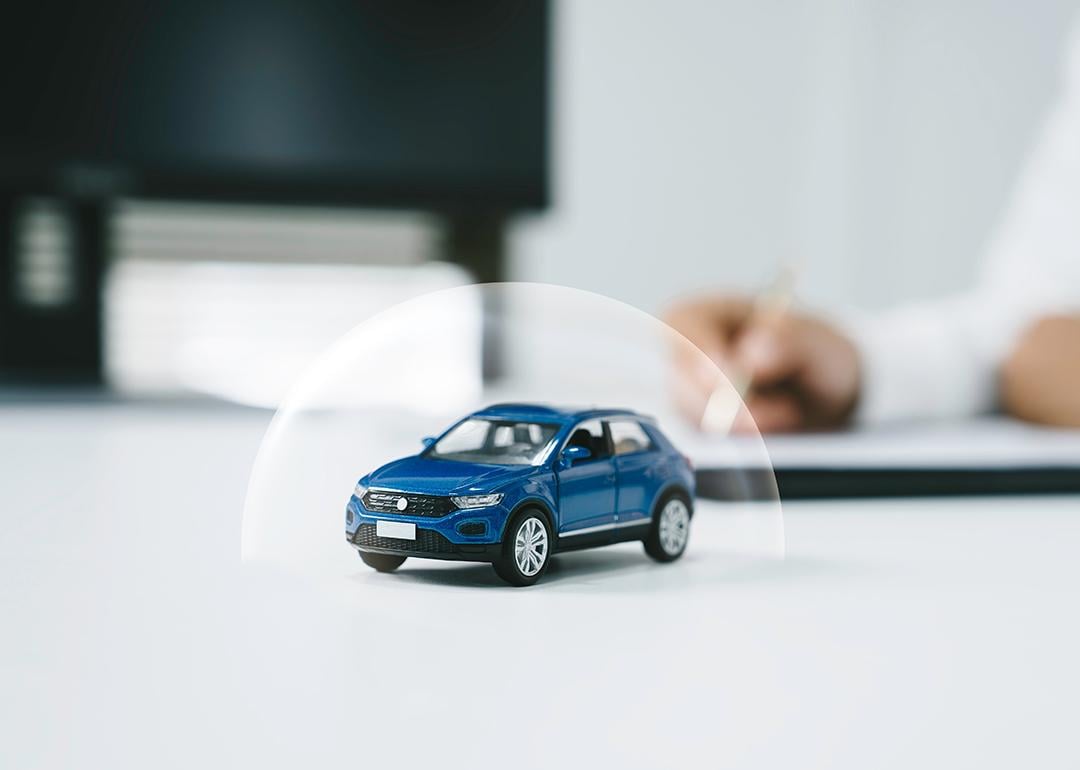 Miniature figure of a blue car with a shield illustration for insurance.