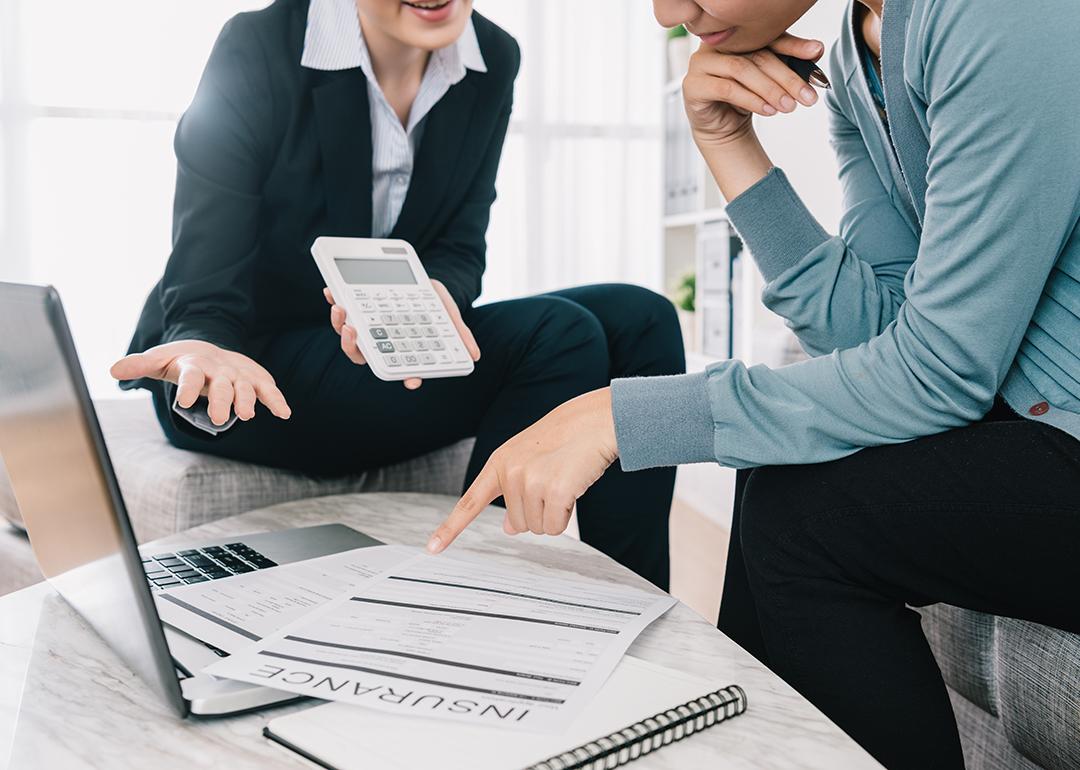 Insurance advisor holding up a calculator while the insurance policy owner reviews documents.