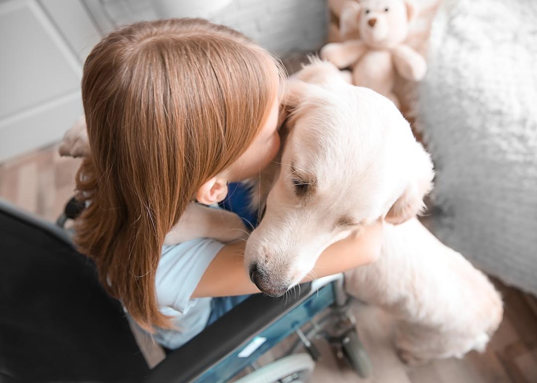 Young girl in wheelchair hugs a service dog.