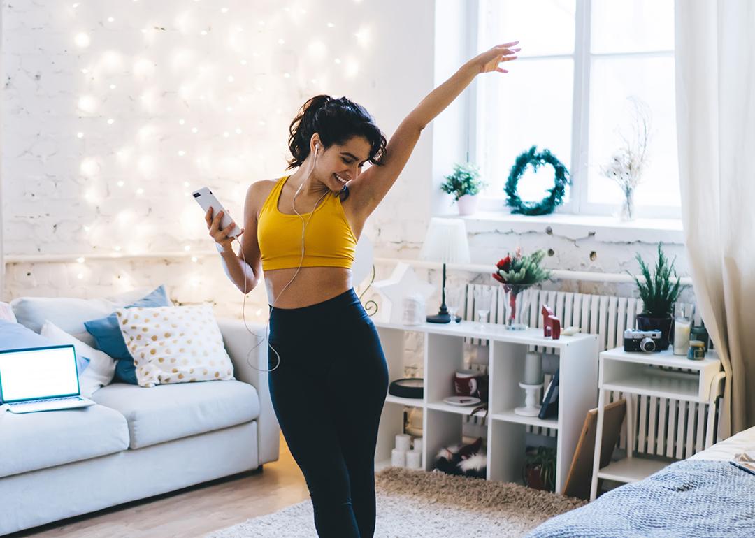 Cheerful young woman dancing to music she is listening to while on a workout at home.