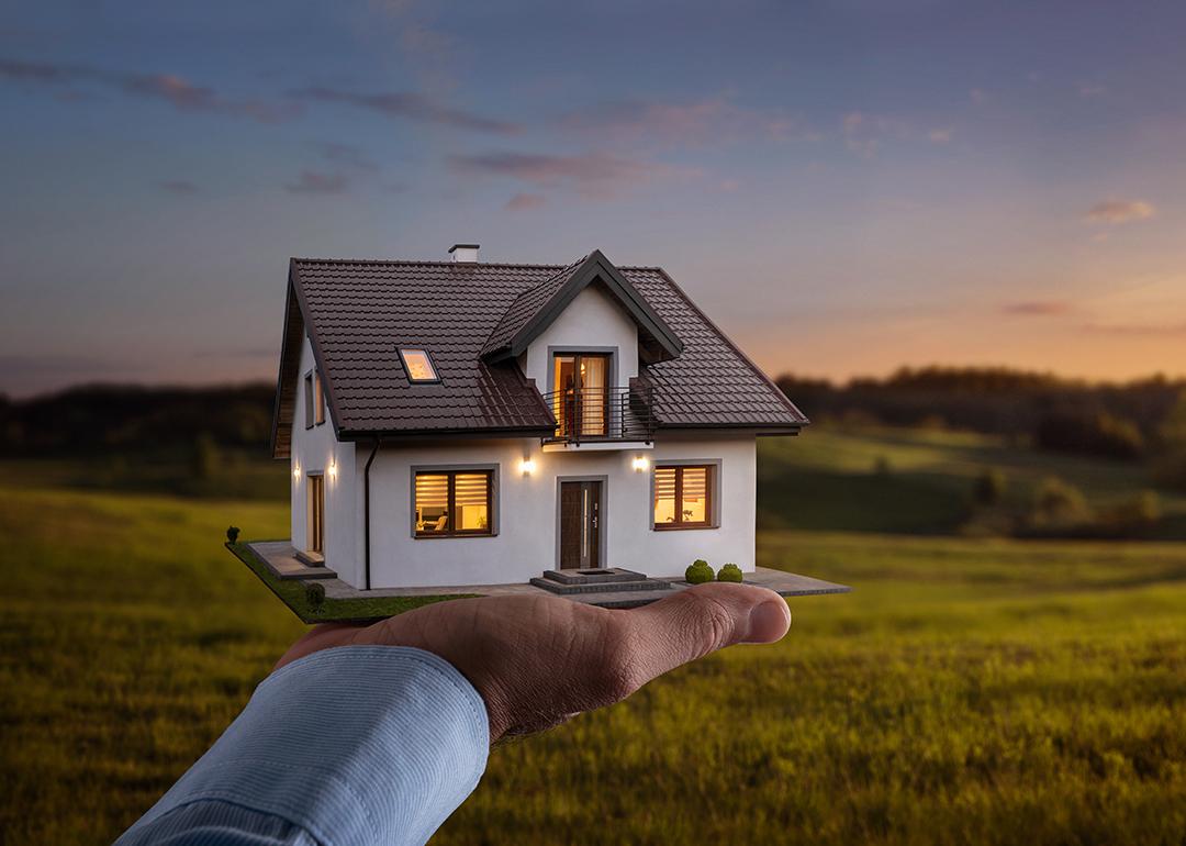 A figure of a house on a person's hand with a sunset background.