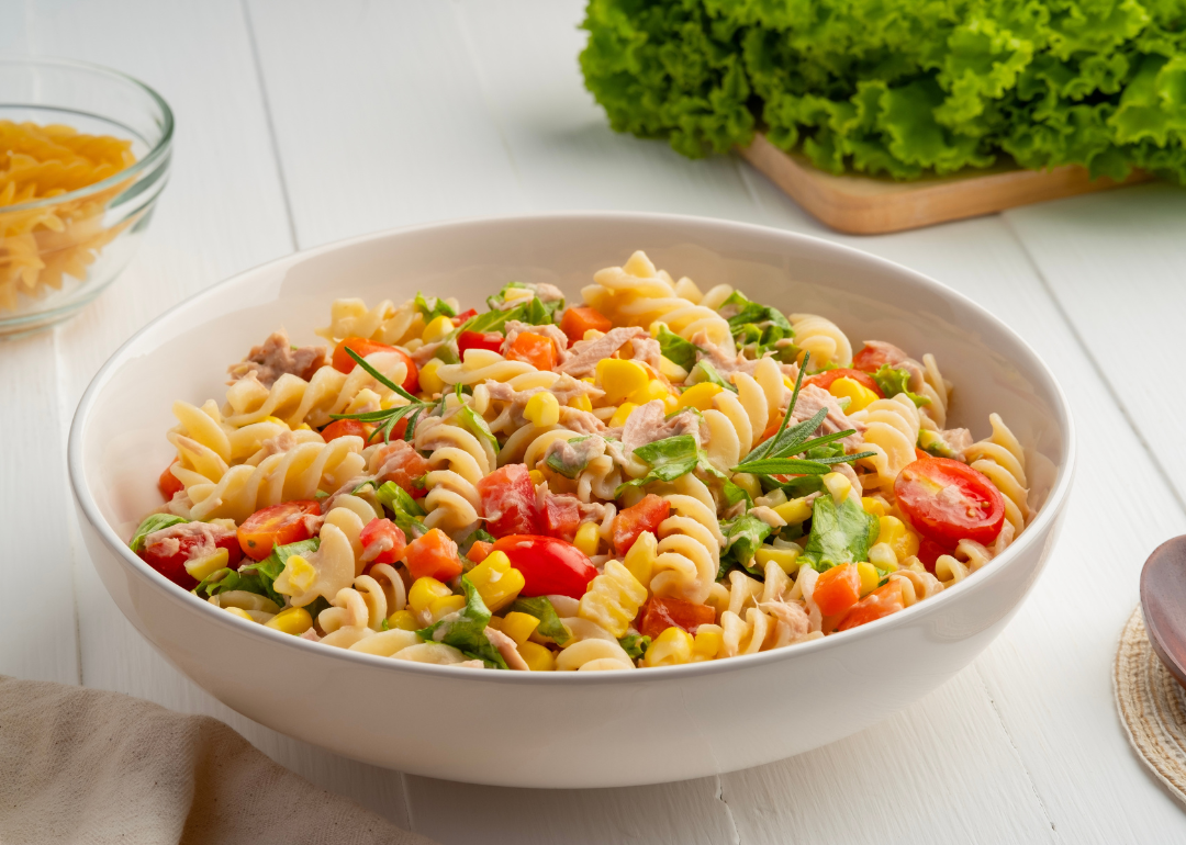 Homemade macaroni salad with trivelle pasta and canned tuna, carrot, lettuce, tomato, corn and mayonnaise dressing in a white plate on wooden table.