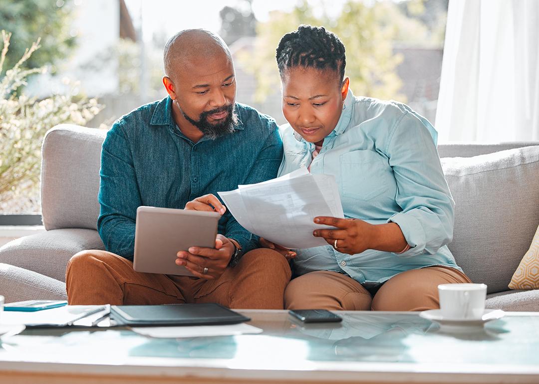 A middle aged black couple reviewing forms and looking up information at home using a tablet.