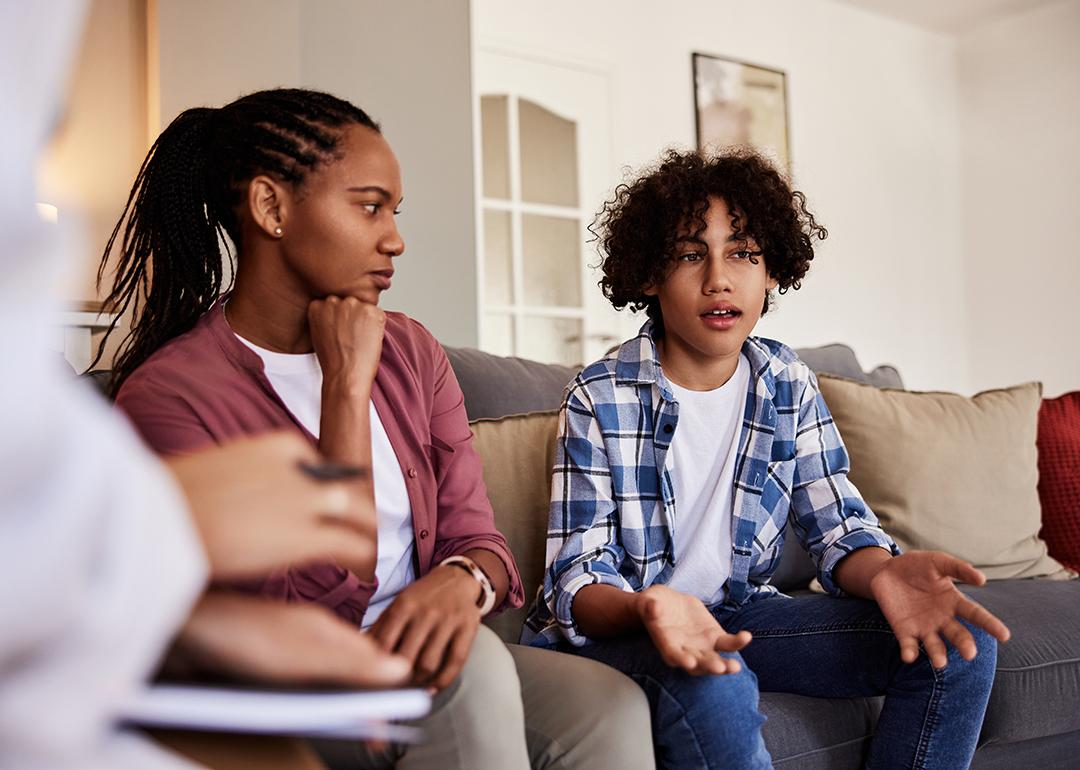 A boy sitting next to his mother in discussion with a doctor in a living room during a home visit.