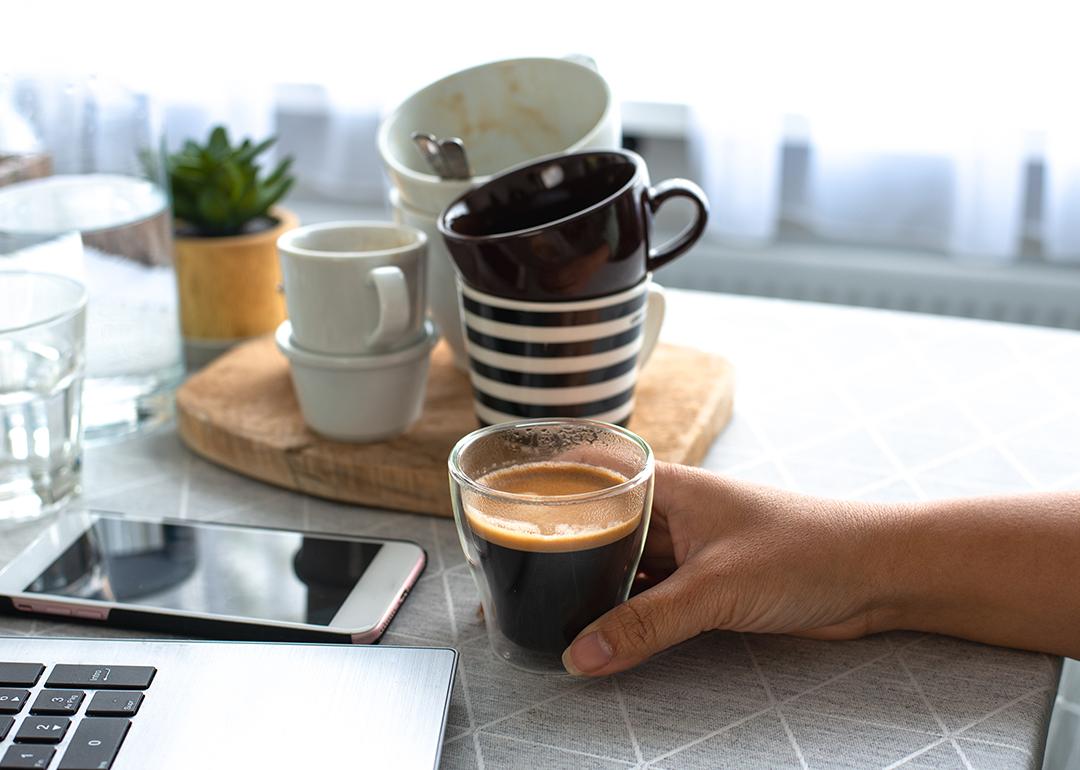 Person holding a full glass of coffee on a background of multiple empty finished cups.