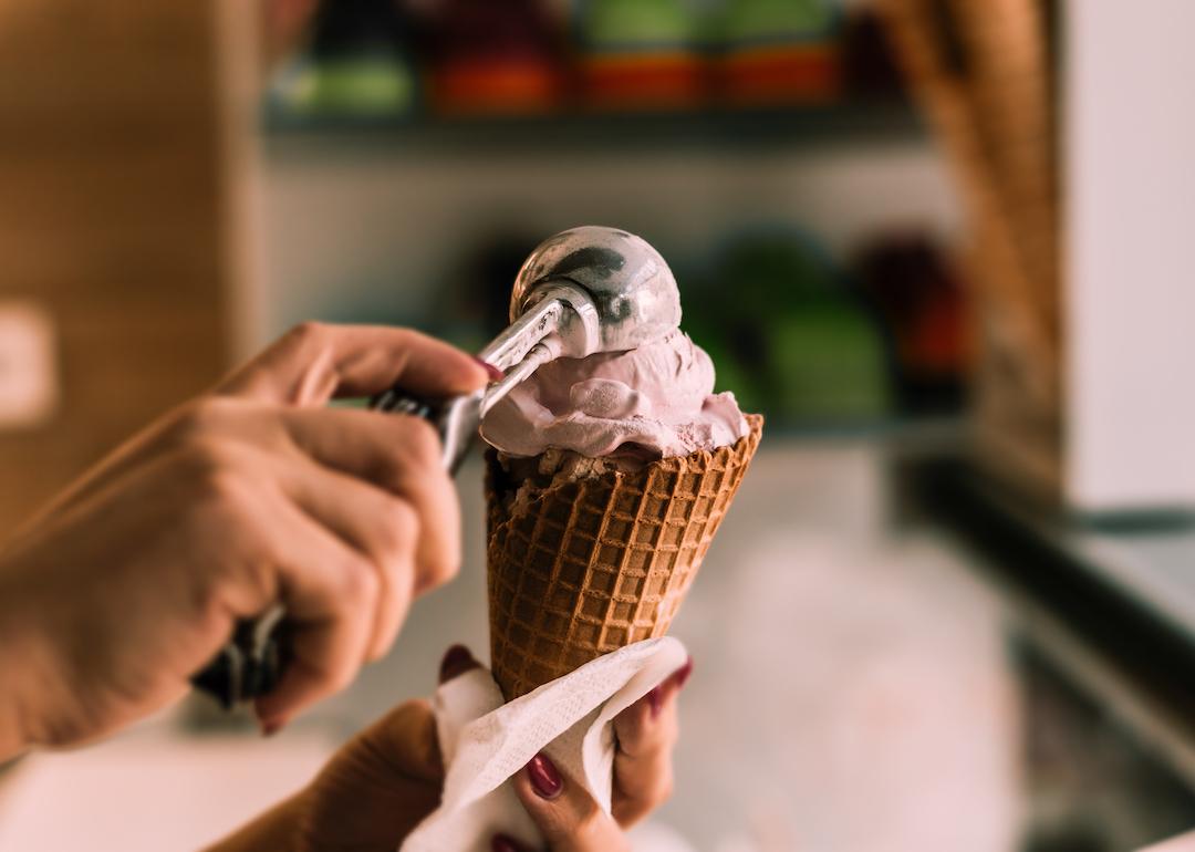 Worker scooping ice cream into waffle cone.