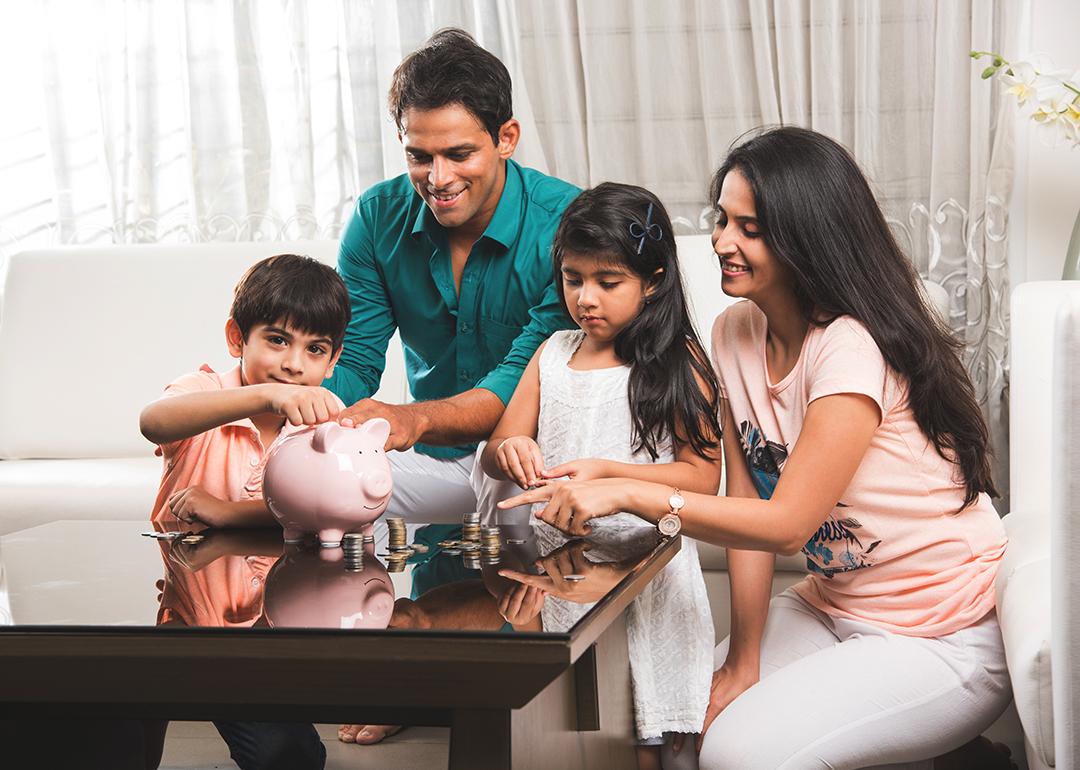 A family of four where parents are teaching their two kids how to save money in a piggybank.