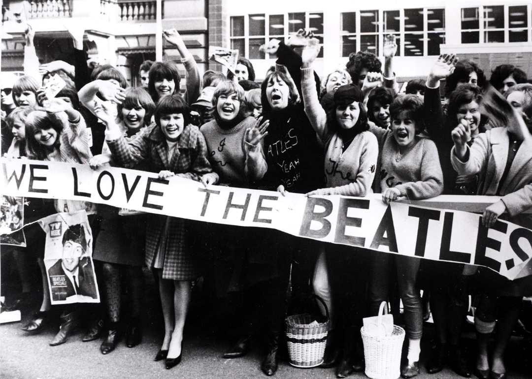 Screaming Beatles fans holding banners and waving at the band, circa 1964