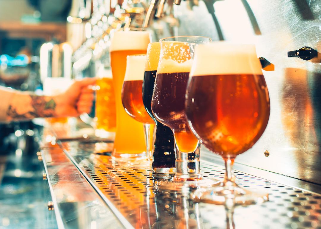 Different types of beer in unique glasses with bartender in background.