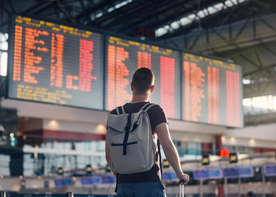 A man with a backpack looking at a departure and arrival schedule board in an airport.
