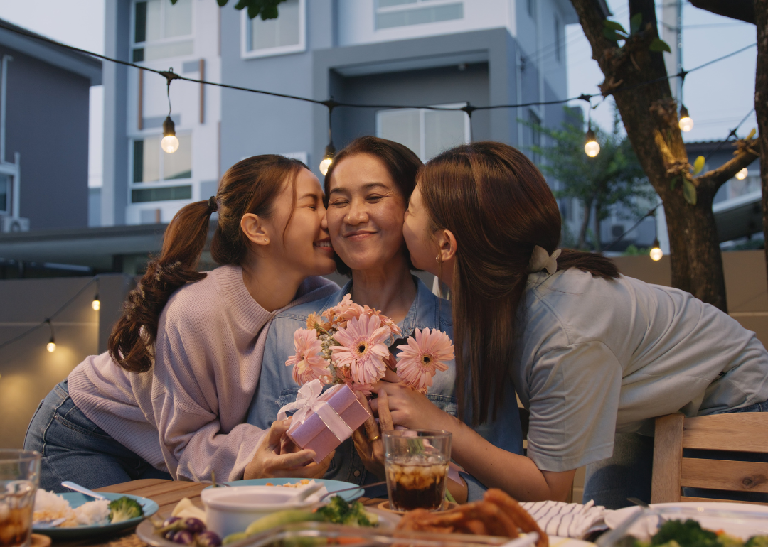 Two children embrace their mother and give her flowers at an outdoor dinner party