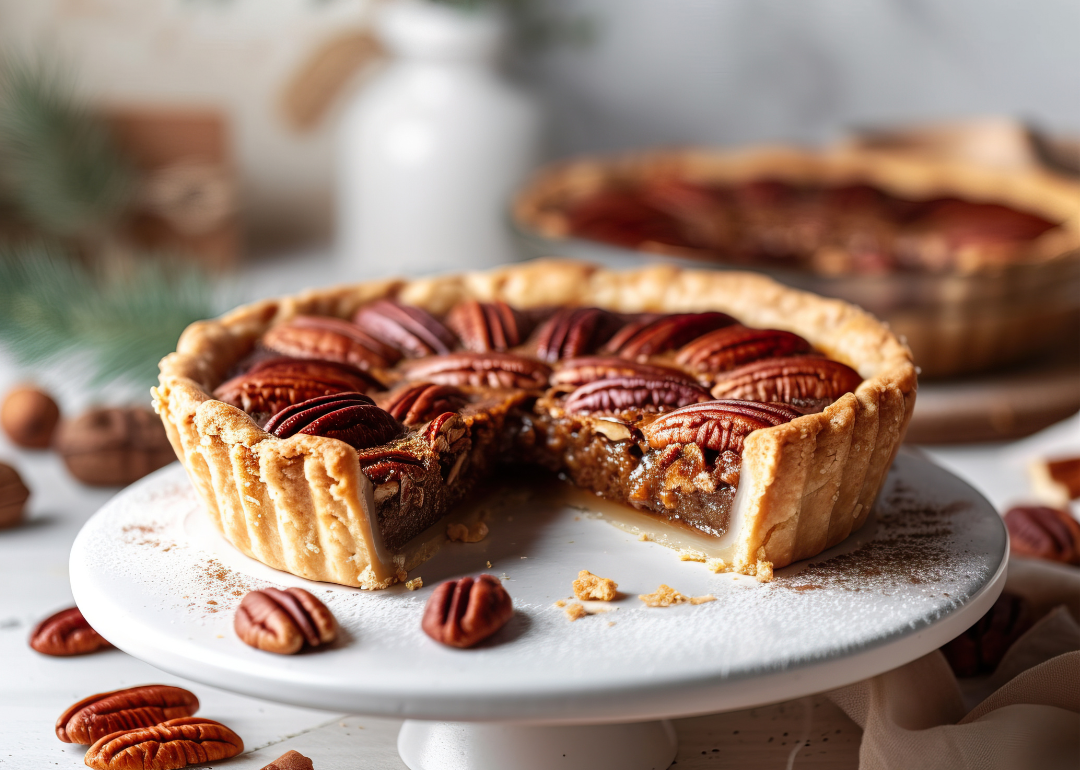 A whole pecan pie with a slice cut out on a white stand