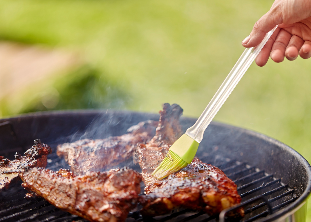 Close up shot of a hand basting barbecue meat on an outdoor grill