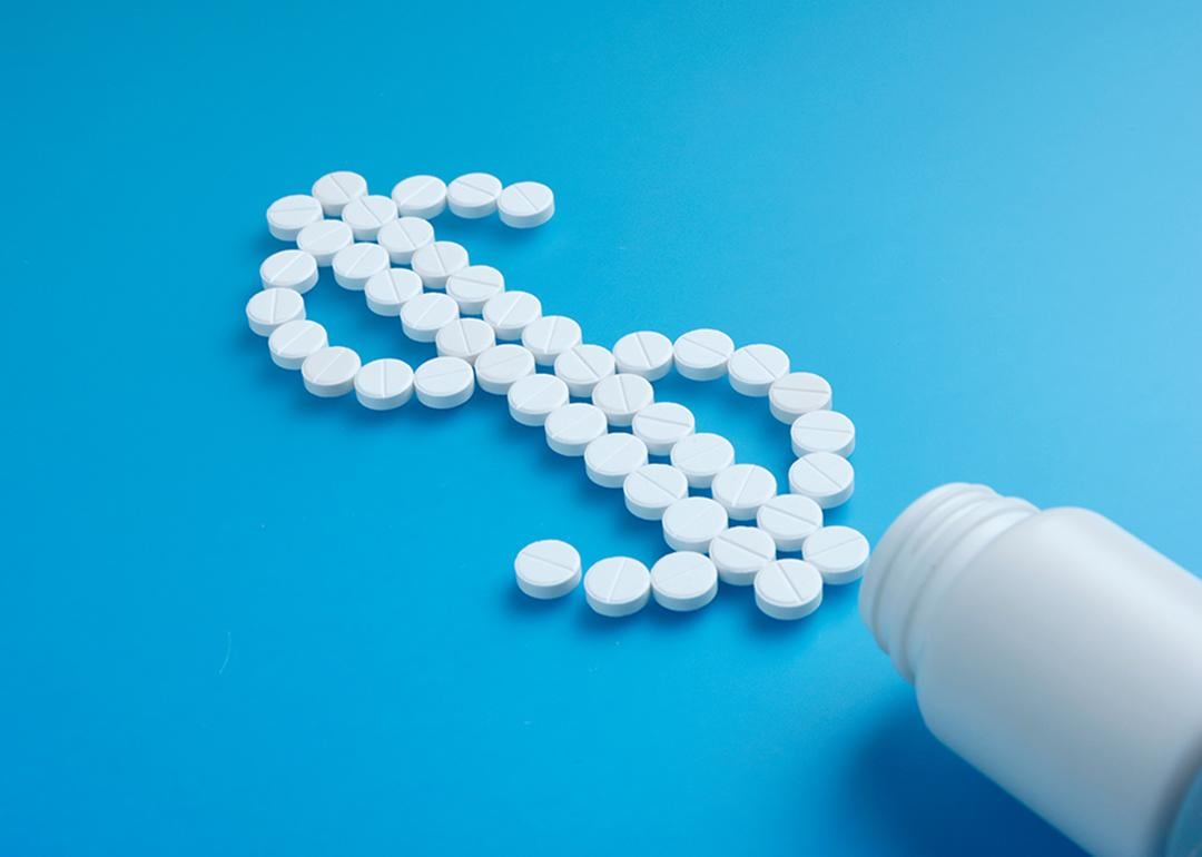 White pills spilling from a bottle forming a dollar symbol.