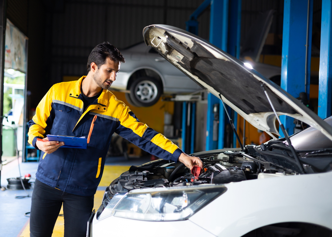 A car maintenance technician inspecting under the hood of a car