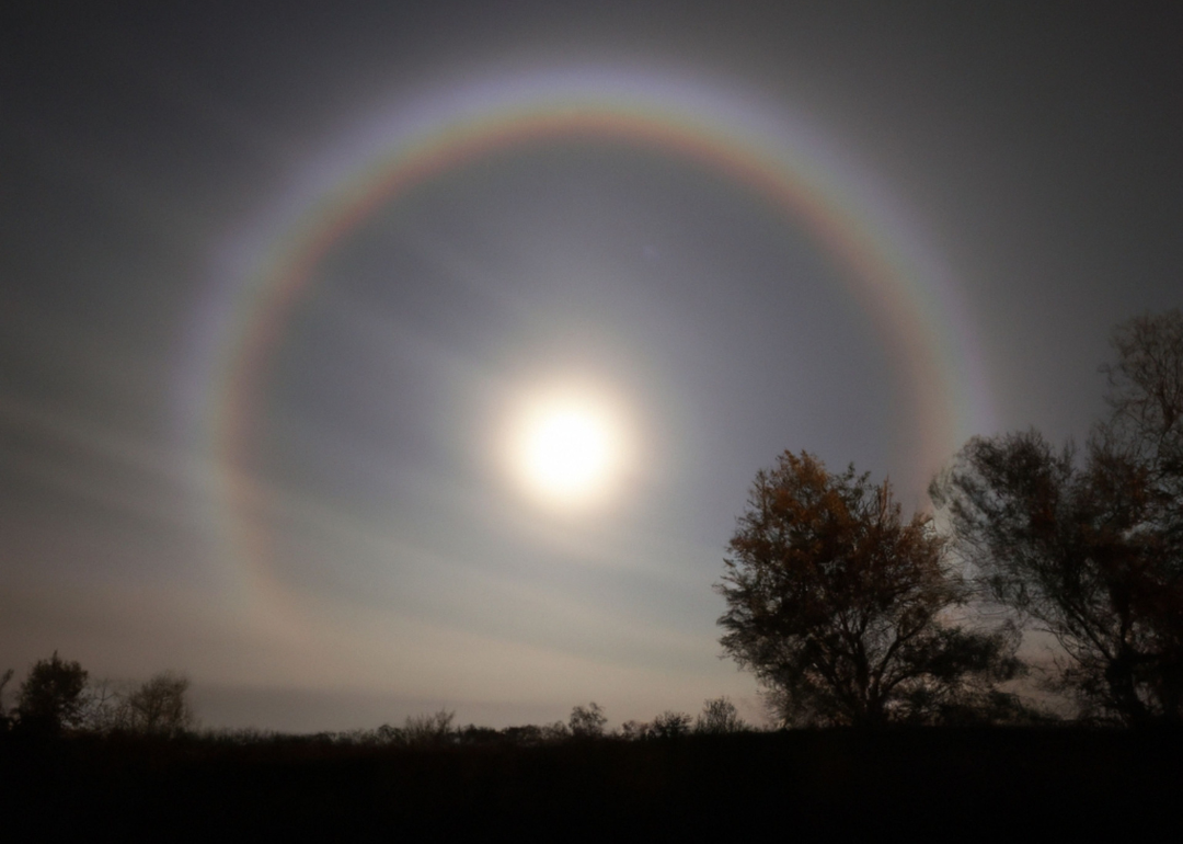 A lunar rainbow and a shining full moon against a clear, dark sky