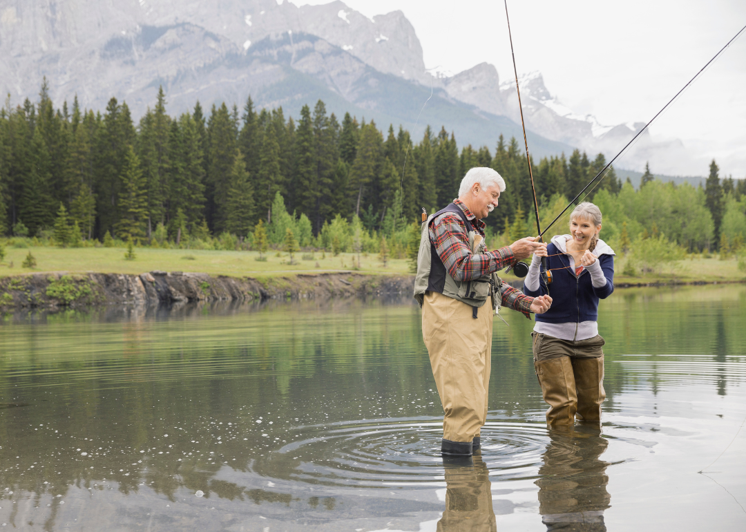 Senior couple standing in an alpine lake with fishing rods