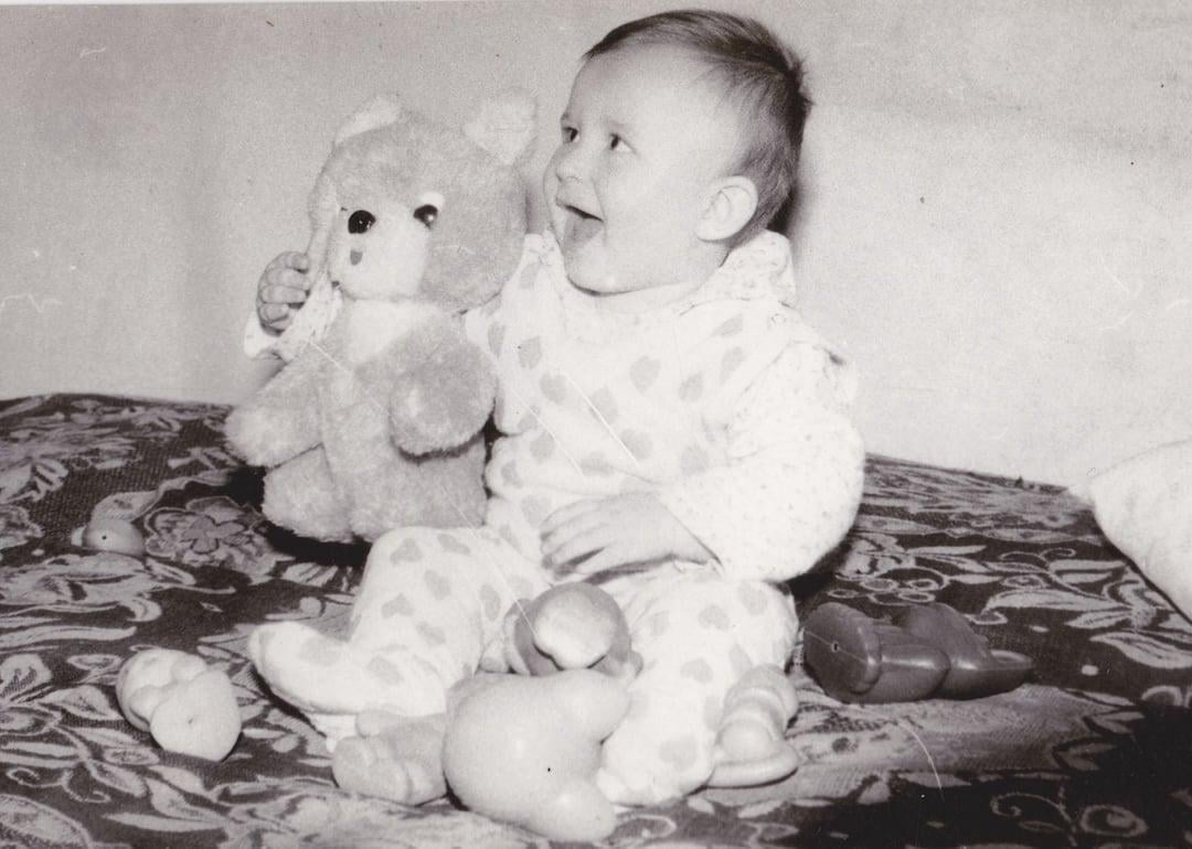 Old cute photo of a baby sitting with toys.