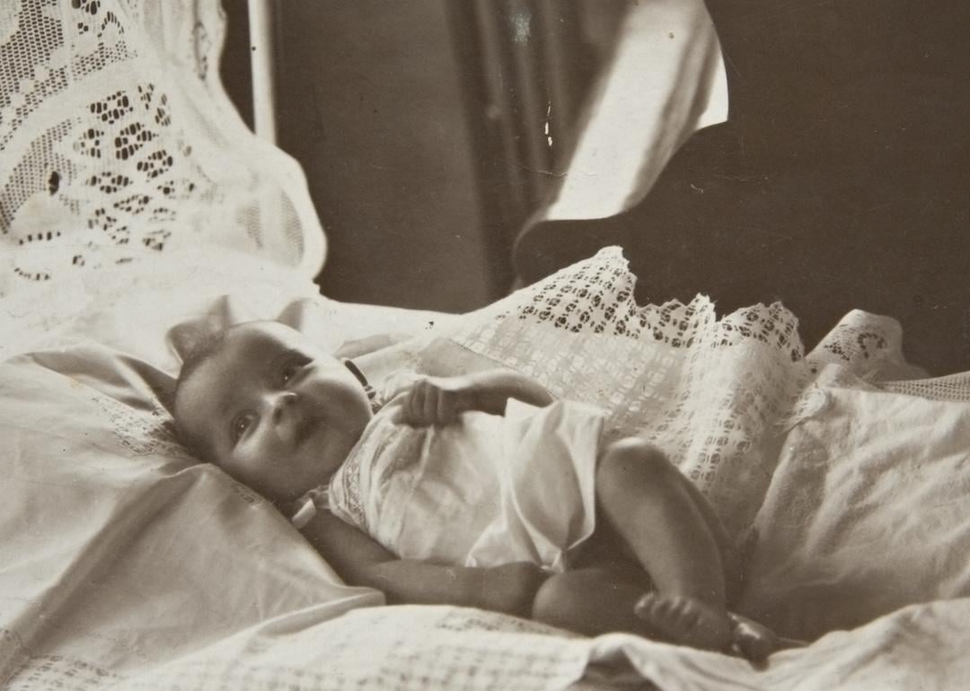 Baby girl laying in bed, circa 1920s.