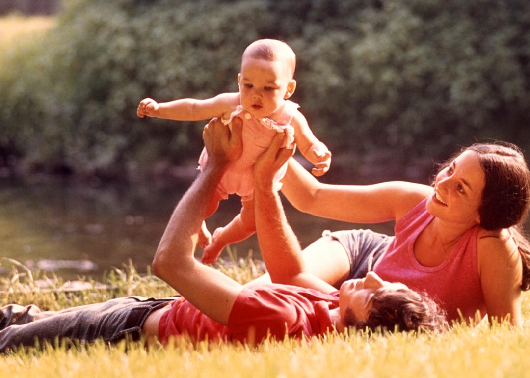 1970s couple laying in the grass holding their baby in the air