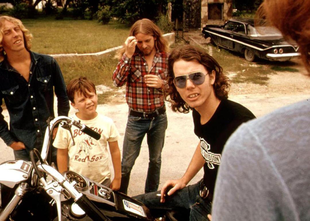 Friends standing around a guy on a motorcycle