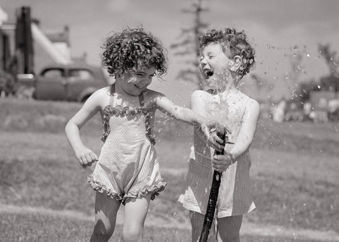 Children in the 1950s splashing water from a garden hose during the summertime.