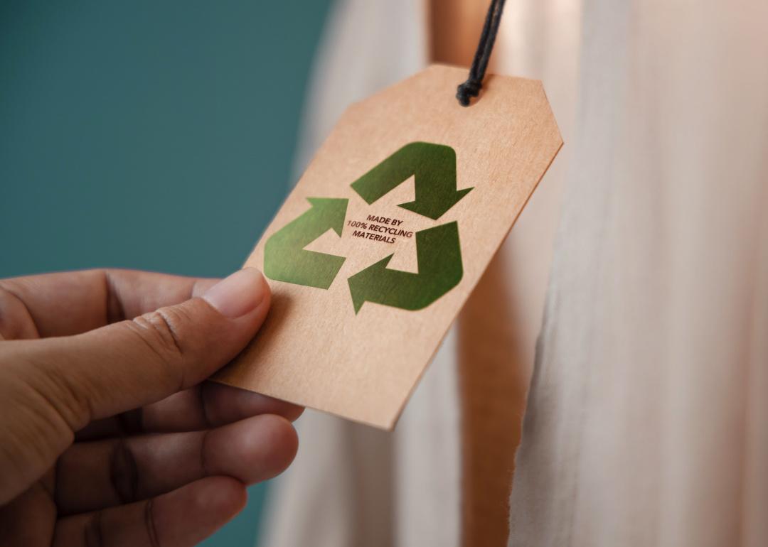 Close up of hand holding a tag that says Made By 100% Recycling Materials attached to a product.