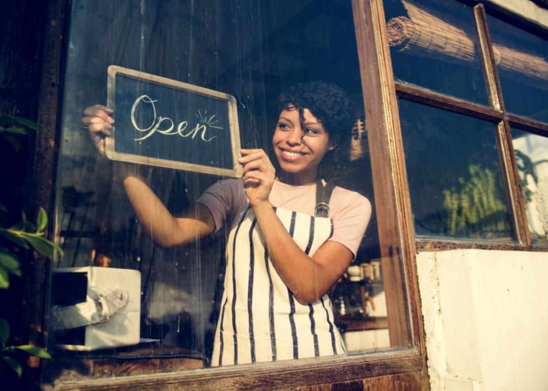 A woman holding an open sign in the window of a business.