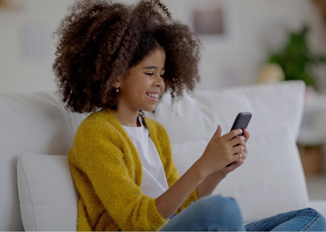 Preteen sitting on the couch at home looking at her cellphone and smiling.