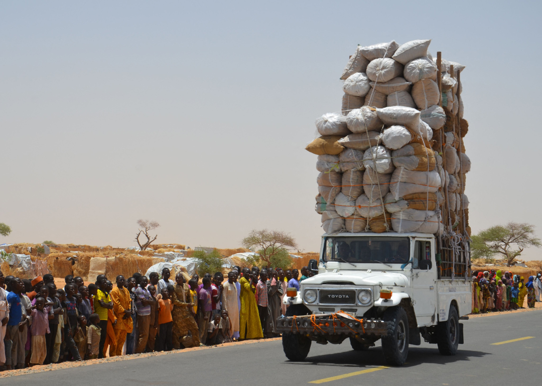 A truck loaded to the sky with donated food next to a street lined with people.