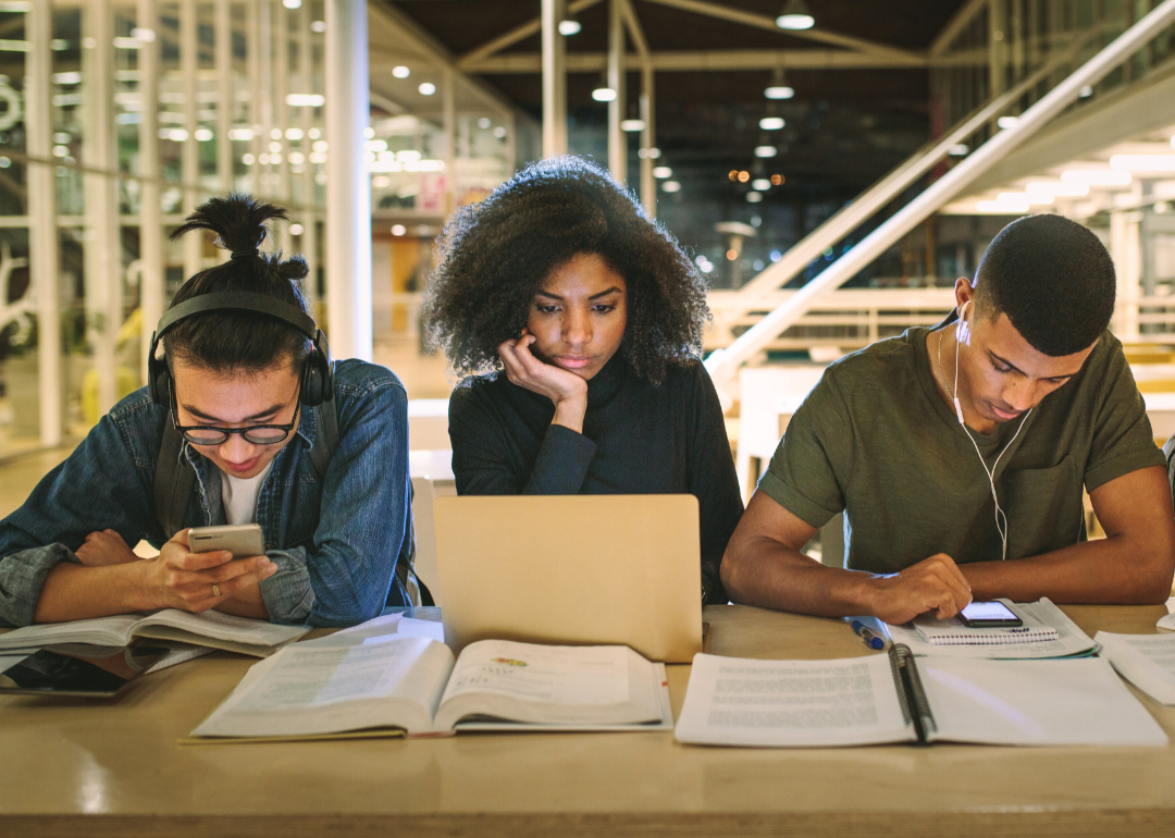 Three college students fixated on their laptops and smartphones.